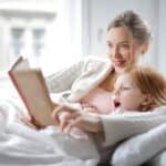 mother and daughter reading book with interest in bed