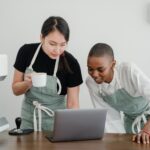 diverse female baristas communicating while using laptop at work