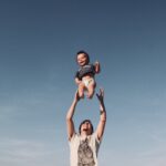 photo of a man raising baby under blue sky
